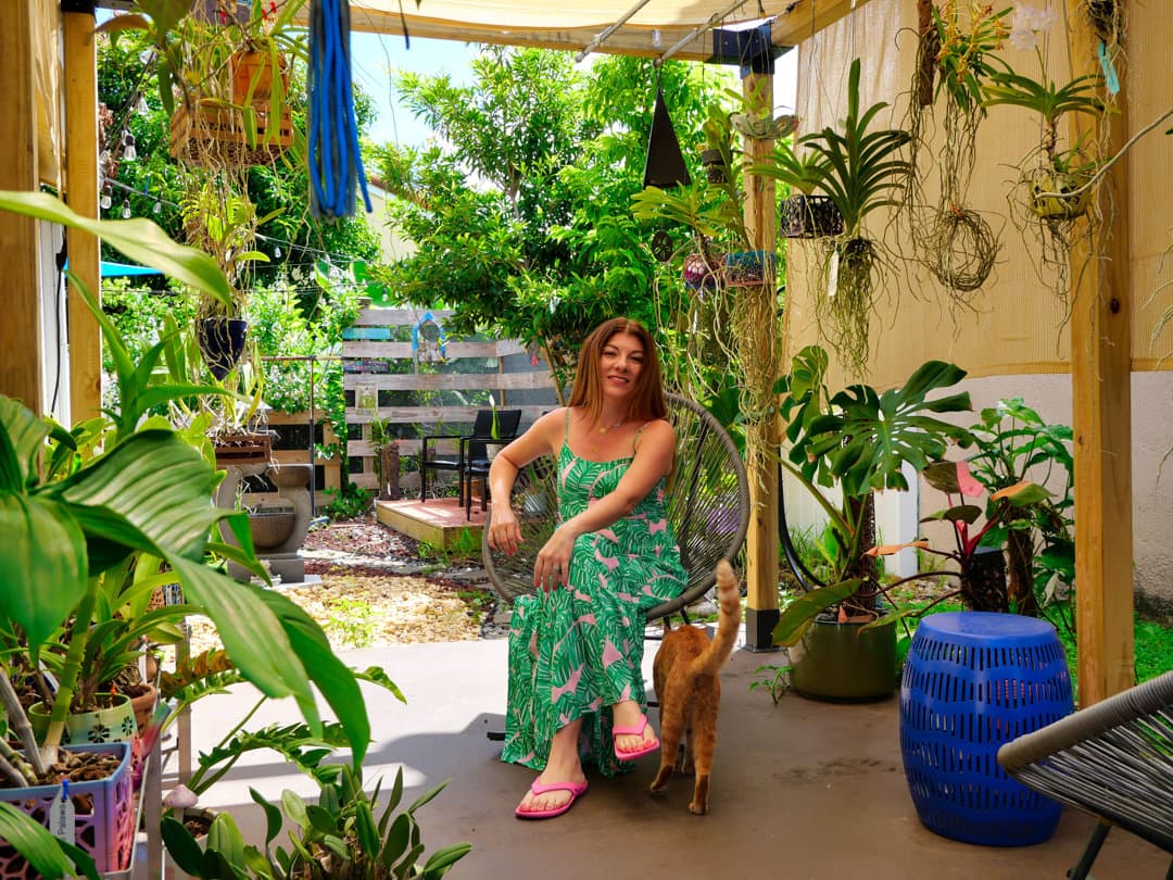 Roxy seated in her lush orchid garden surrounded by hanging plants and monstera